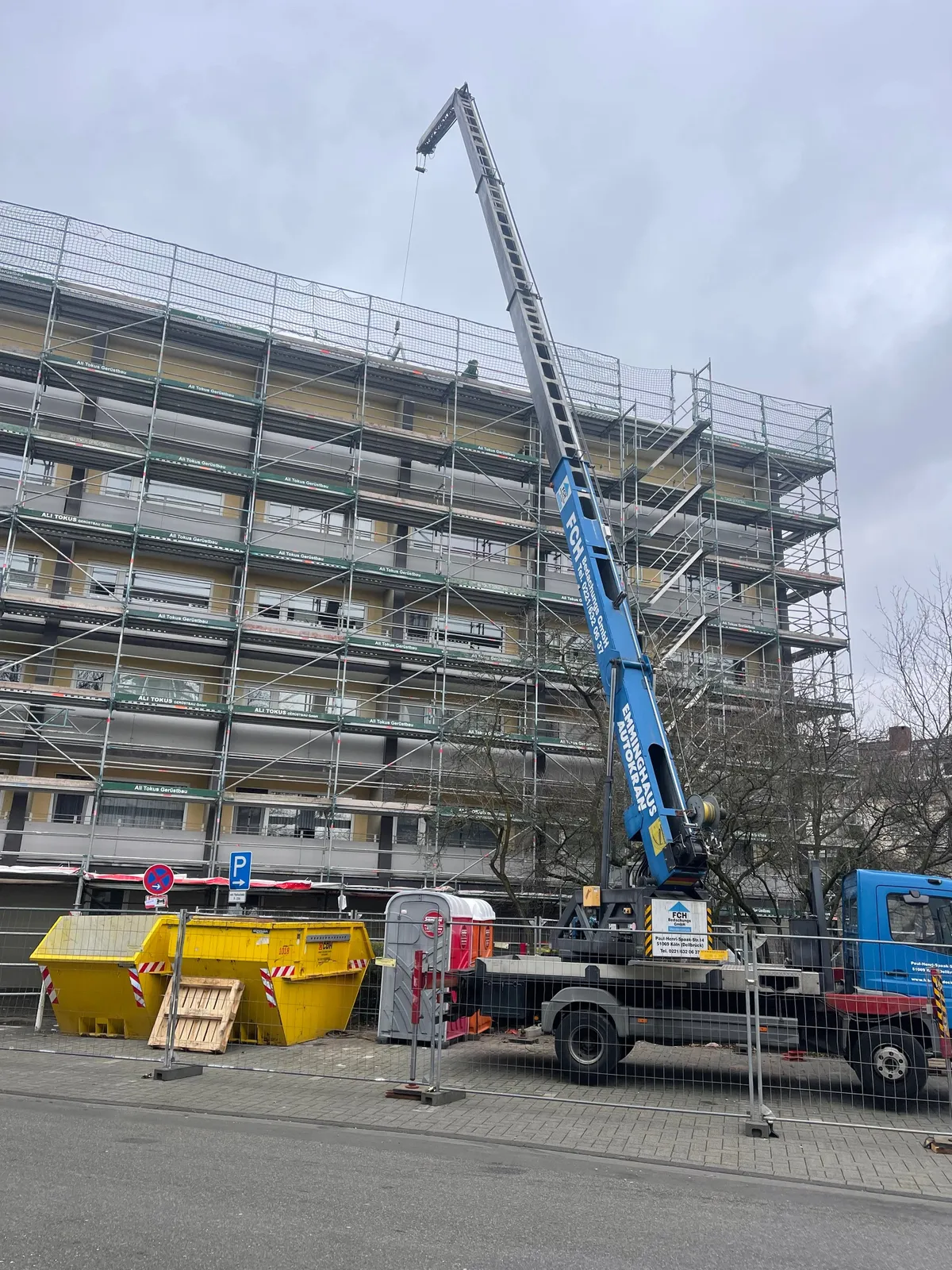 FCH-Kran vor einem eingerüsteten Mehrfamilienhaus.